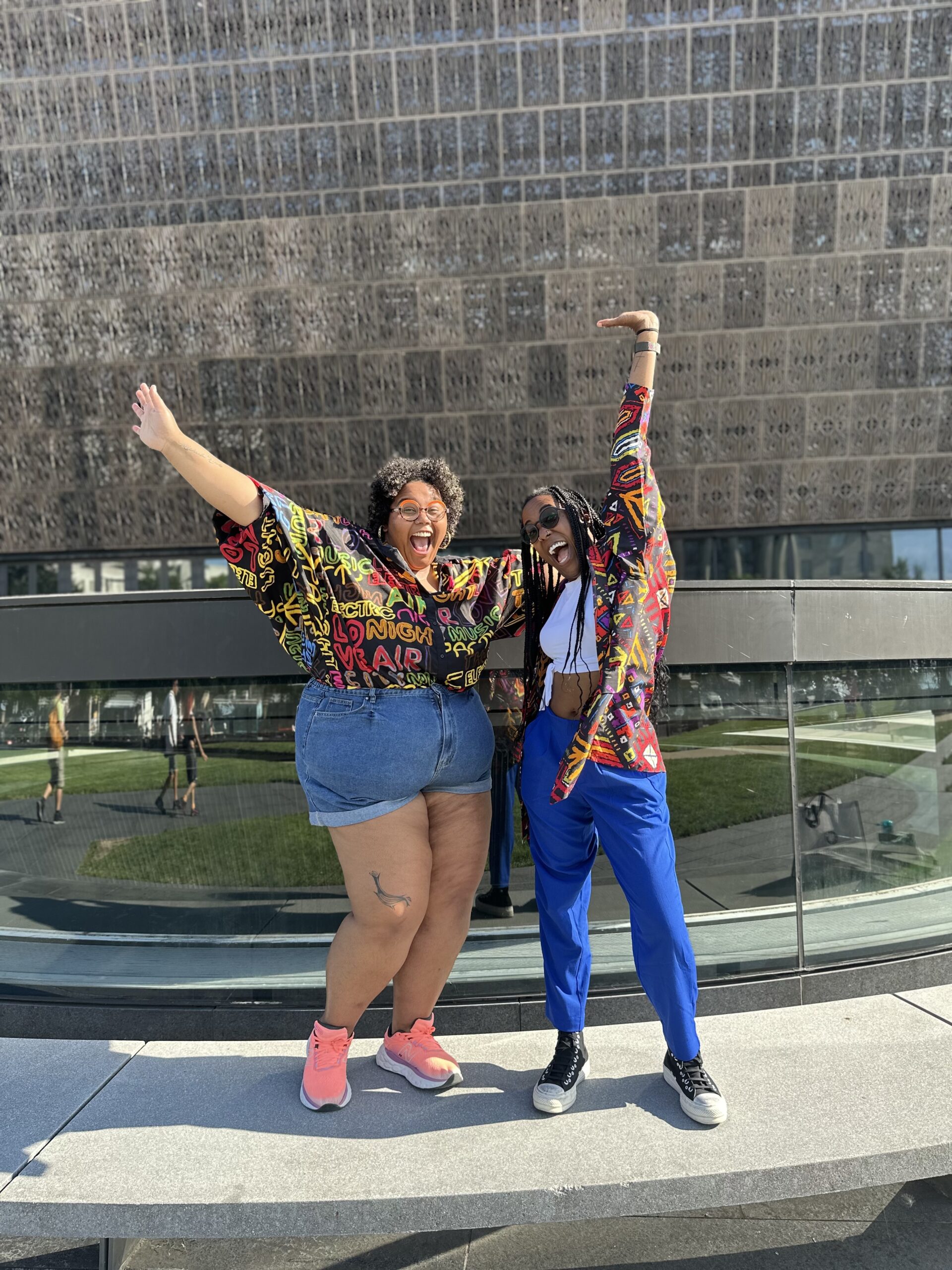 Courtney and Ash stand in front of a wall in an excited energetic pose.